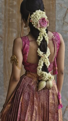 a woman with flowers in her hair is wearing a pink dress and holding a flower garland