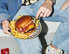 a woman is holding a plate with a sandwich and french fries in her lap while sitting down