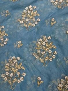 a blue and gold embroidered fabric with white flowers on the side, surrounded by small beads