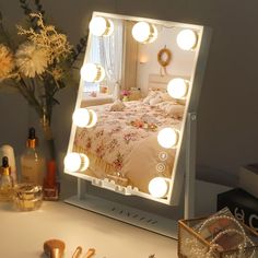 a lighted vanity mirror sitting on top of a white table next to a vase with flowers