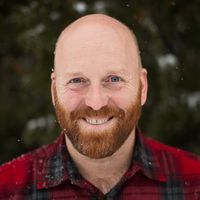 a man with a bald head wearing a red plaid shirt and smiling at the camera