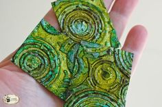 a hand holding a piece of art made out of green and yellow paper with spiral designs on it