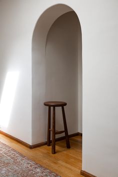 a wooden stool sitting next to a white wall in a room with wood flooring