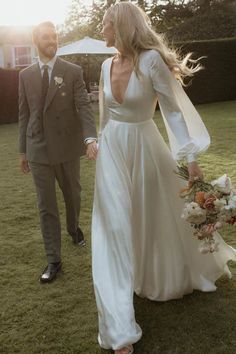 a bride and groom walking in the grass holding hands at their outdoor wedding ceremony with an umbrella behind them