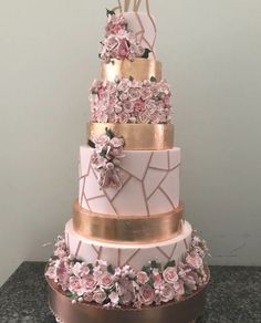 a three tiered cake with pink flowers and gold trimmings on a table