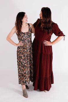 two women standing next to each other in front of a white background, one wearing a brown dress