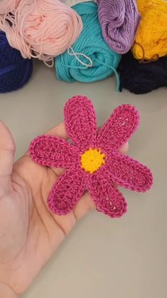 a hand holding a crocheted flower in front of several balls of yarn