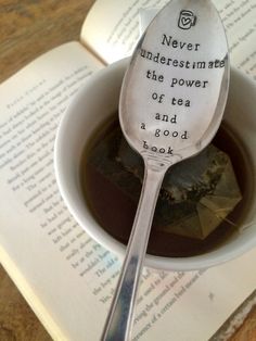 a spoon that is sitting in a cup on top of an open book with the words never underestimate the power of tea and a good book