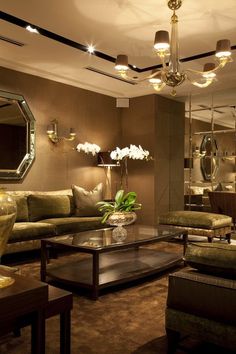 a living room filled with lots of furniture next to a wall mounted mirror and chandelier