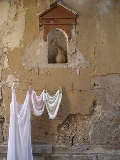 clothes hanging out to dry in front of a stone wall with a window and birdhouse