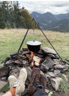 a person sitting in front of a campfire with a pot on it