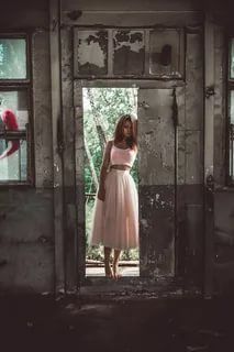 a woman in a pink dress is standing in an abandoned building