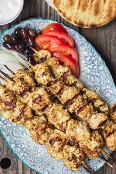 chicken skewers with tomatoes, onions and olives on a plate next to pita bread