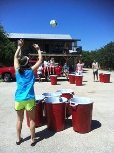 a girl throwing a ball into buckets in front of a house with other people