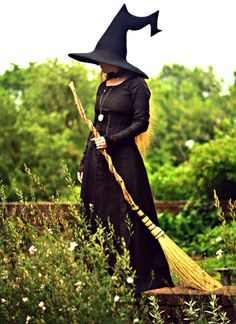 a woman dressed as a witch with a broom in her hand and wearing a black dress