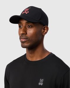 Maxwell wore a 100% cotton black long-sleeve shirt with a small white bunny logo on the chest and topped it off with the MENS MAXWELL SPORT CAP - B6A783D200 by Psycho Bunny, featuring a red skull and crossbones emblem. The background was plain gray. Black Curved Visor Dad Hat For Sports Events, Black Dad Hat For Sports Events, Sporty Cotton Fitted Hat For Sports, Black Trucker Hat With Curved Visor For Sports Events, Sporty Cotton Fitted Hat, Breathable Cotton Sports Baseball Cap, Breathable Cotton Baseball Cap For Sports, Casual Black Breathable Fitted Hat, Black Fitted Hat For Outdoor With Curved Visor