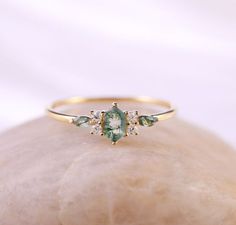 a close up view of a ring with green and white stones on the front, sitting on top of a rock