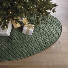 a christmas tree with presents under it on a green rug next to a white box