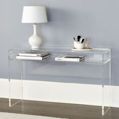 a clear console table with two books on it and a lamp next to it in a living room