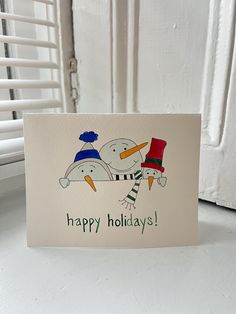 a white card with a snowman and penguin on it that says happy holidays next to a radiator