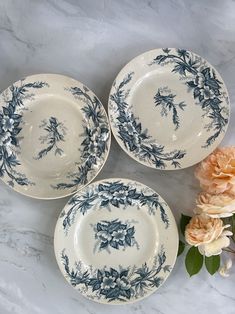 three blue and white plates sitting on top of a table next to some pink flowers