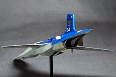 a blue and white fighter jet model on a black stand with grey background in the foreground