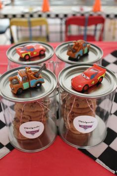 four tins filled with cookies and cars on top of a checkered table cloth