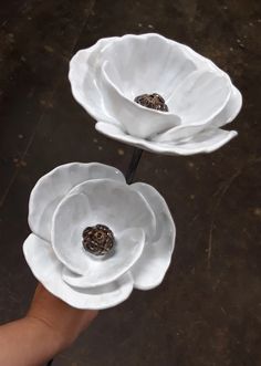 two white flower shaped dishes sitting on top of each other in front of a person's hand