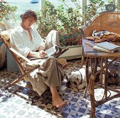 a woman sitting in a chair next to a dog on the floor with a book