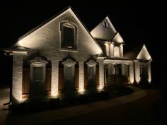 a house that is lit up at night with lights on the front and side of it