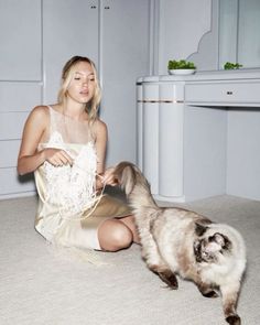 a woman sitting on the floor next to a cat and playing with it's tail