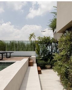 an outdoor patio with benches and plants next to a pool in front of a building