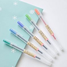 six pens are lined up in a row on top of a blue notebook with snowflakes