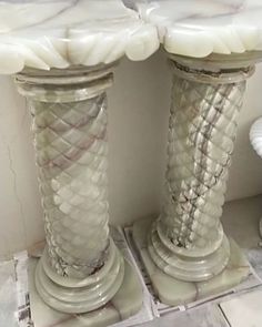 two white vases sitting next to each other on top of a tile floor in front of a wall