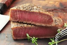 two pieces of meat sitting on top of a cutting board next to a knife and fork