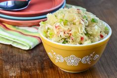 a yellow bowl filled with coleslaw sitting on top of a wooden table next to plates