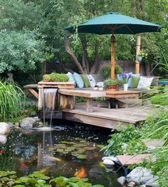 a small pond in the middle of a garden with a deck and umbrella over it