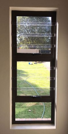 a window with blinds on the outside and inside, looking out at a yard in front of it