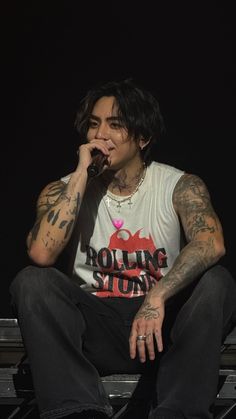 a man sitting on top of a stage while holding a microphone to his mouth with both hands