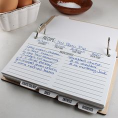 an open recipe book sitting on top of a table next to eggs in a bowl