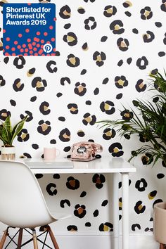 a white table topped with a plant next to a wall covered in black and gold spots