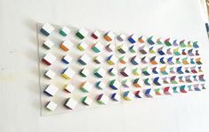 there are many different colored paper shapes on the white wall, and one has a pencil next to it