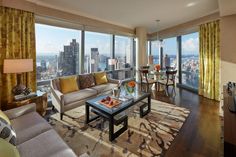 a living room filled with furniture and large windows overlooking the cityscape in the distance