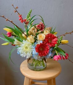 a vase filled with flowers sitting on top of a wooden stool next to a wall