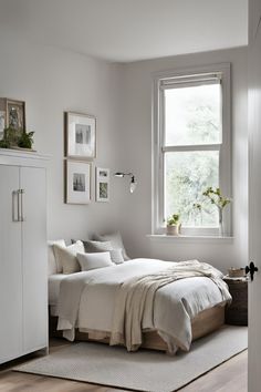 a bedroom with white walls and wooden flooring is pictured in this image, there are pictures on the wall above the bed