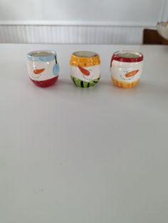 three small cups sitting on top of a white table next to each other and one has a bird painted on it