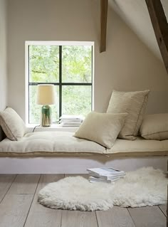 a white bed sitting under a window next to a wooden floor covered in pillows and blankets