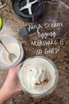 a person holding a glass with whipped cream in it next to other cups and spoons