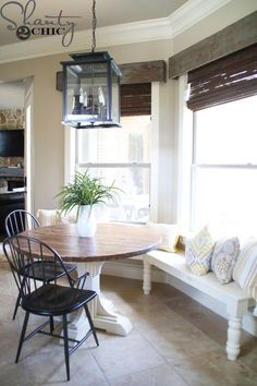 a dining room table with two chairs and a bench in front of the bay window