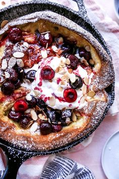 a baked dessert in a cast iron skillet with berries and almonds on top